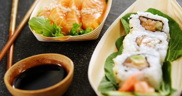 Close-up view of fresh sushi and sashimi platter featuring salmon sashimi garnished with sesame seeds, sushi rolls with rice and fish fillings, and a bowl of soy sauce. Ideal for illustrating concepts of Japanese cuisine, food photography, restaurant menus, and healthy eating.