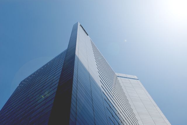 Tall, modern high-rise office building with a sleek glass facade against a clear, sunny sky. This image captures the essence of corporate and urban environments and is ideal for use in business presentations, corporate website banners, real estate brochures, and architectural firm portfolios. The stark minimalism and contemporary design emphasize roof strength, economic growth, and professional business atmospheres.