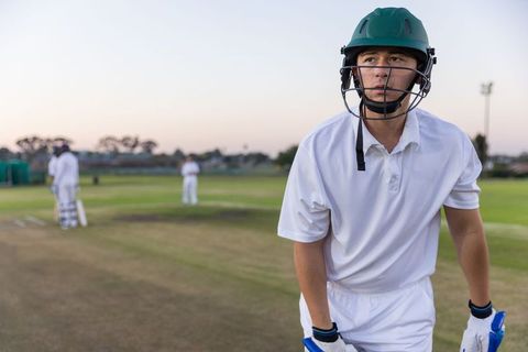 Young batsman leaning on crease wearing green helmet and gloves during dusk cricket match