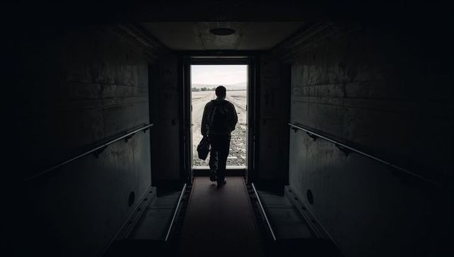 Walking silhouette traveler heading toward bright doorway carrying duffel bag