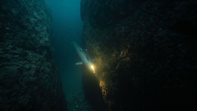 Torpedo rov navigating deep underwater crevasse casting bright beam on rocky walls