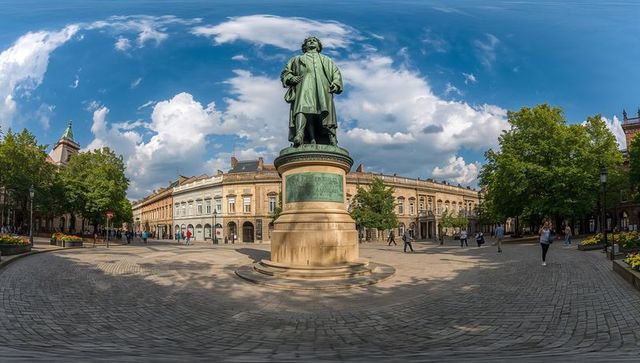 Standing bronze statue anchoring historic european city square under dramatic blue sky