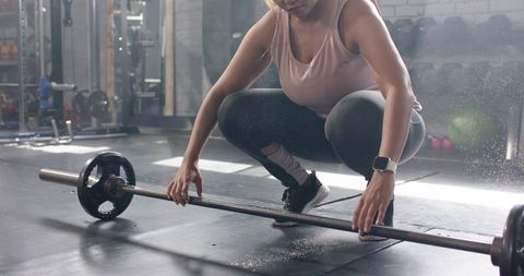 Female weightlifter squatting setting loaded barbell on rubber gym floor with chalk dust