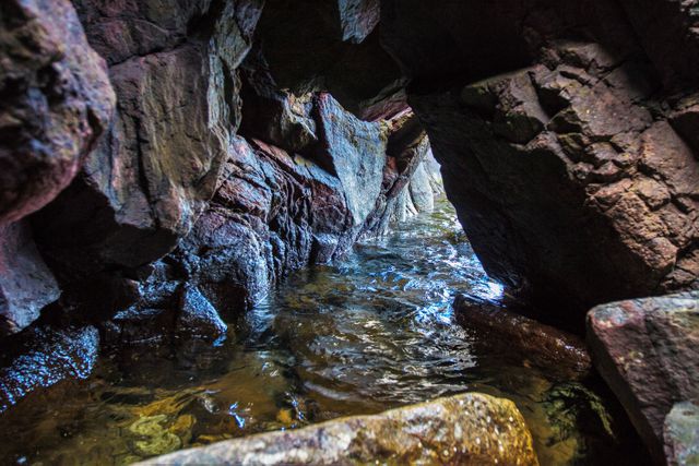 Depicting the entrance of a coastal cave, the image captures sunlight illuminating the rugged rocks and water flowing beneath. Perfect for use in travel blogs, adventure-themed websites, geological studies, and nature photography collections, highlighting natural beauty and rock formations.