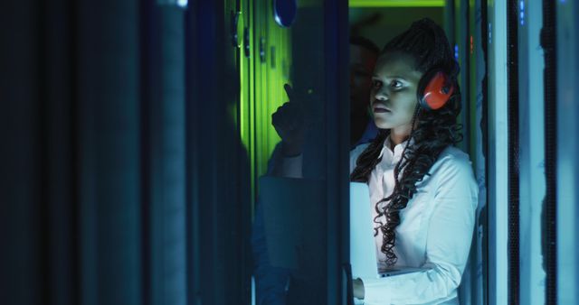 African American woman wearing headphones and focused on computer maintenance. Ideal for illustrating tech workplaces, data management, and network support roles.