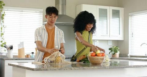 Diverse couple unpacking groceries and arranging fresh produce on marble kitchen island