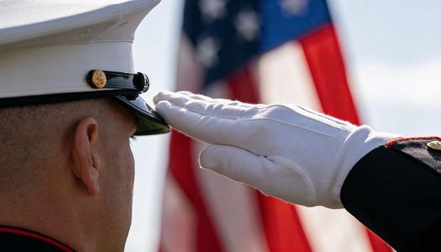 Marine saluting in white dress cap and glove with blurred american flag backdrop