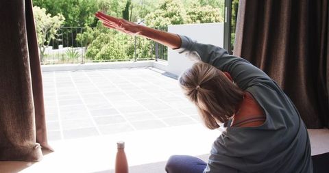 Senior woman enjoying stretching exercise near patio door