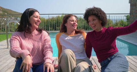 Smiling friends relaxing on sunny backyard pool deck laughing and enjoying summer