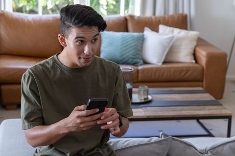 African american man using smartphone on sofa in modern living room, casual moment
