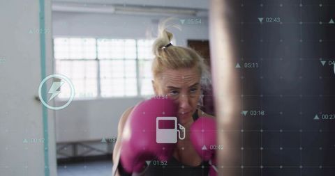 Female boxer training with digital hud overlay punching heavy bag in bright boxing gym