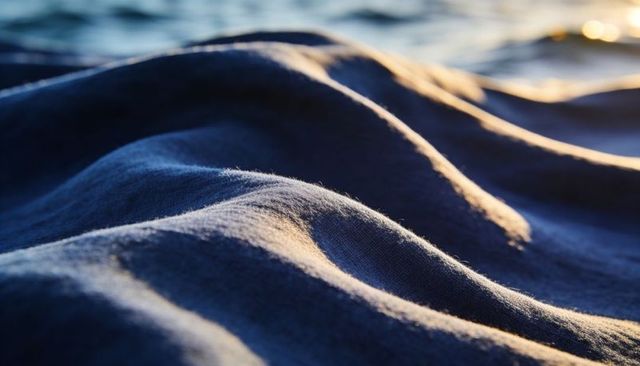Sunlit navy fabric forming soft folds with golden highlights near calm water