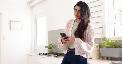 Woman in Bright Kitchen Checking Smartphone Near Cooktop