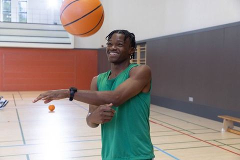 Smiling african american athlete tossing basketball on indoor gym court in green jersey