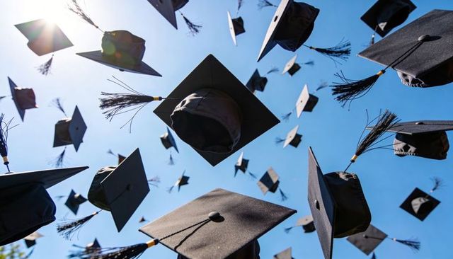 Caps soaring into blue sky with sun flare and tassels celebrating graduation