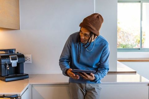 African american man leaning on counter using tablet beside coffee machine in modern kitchen