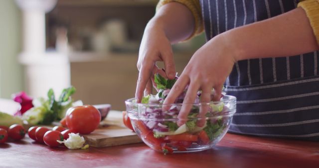 Person preparing a fresh vegetable salad in a kitchen, focusing on hands. Ideal for use in articles or advertisements related to healthy eating, cooking tutorials, nutrition tips, culinary blogs, and organic food lifestyle promotions. The vibrant colors of the vegetables enhance the freshness and appeal of the scene.