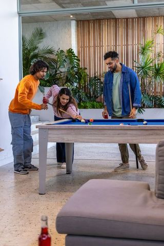 Friends playing pool in modern lounge with blue-felt table and indoor plants