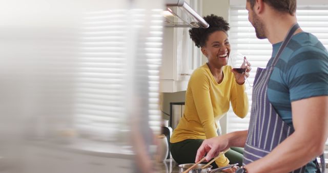 Image of happy diverse couple preparing meal, drinking wine and having fun in kitchen. Love, relationship and spending quality time together at home.