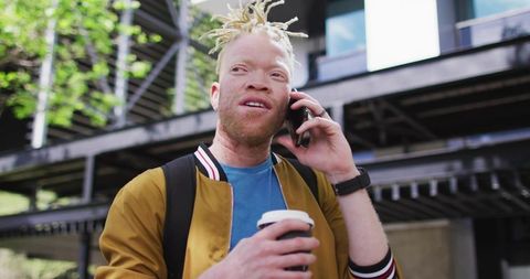 Albino man having phone call holding coffee outside modern building