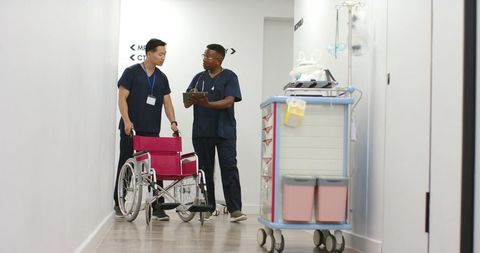 Healthcare team discussing patient transfer with red wheelchair and medical cart