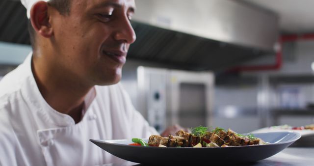 Caucasian male chef garnishing dish and smiling in restaurant kitchen. Working in a busy restaurant kitchen.