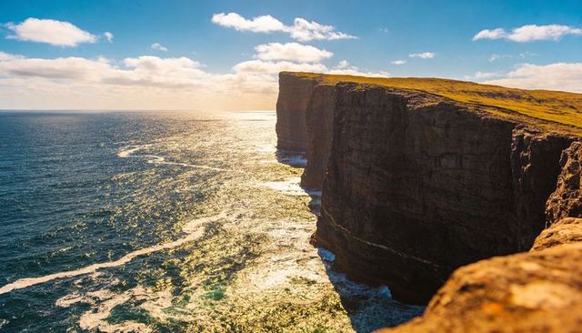 Sunlit Rugged Sea Cliffs Overlooking Turquoise Ocean Waves on Windswept Grassy Plateau