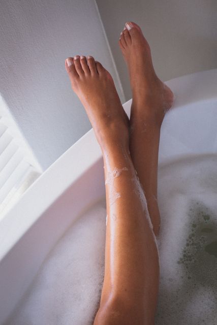 Legs of biracial woman relaxing in the bath with her feet up. staying at home in isolation during quarantine lockdown.