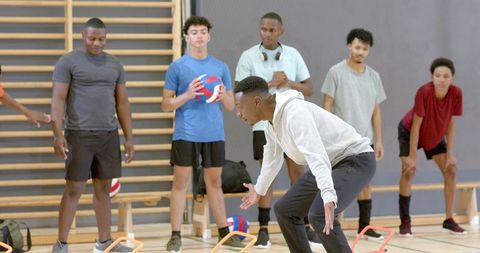 High school volleyball team training agility drills with coach in indoor gymnasium