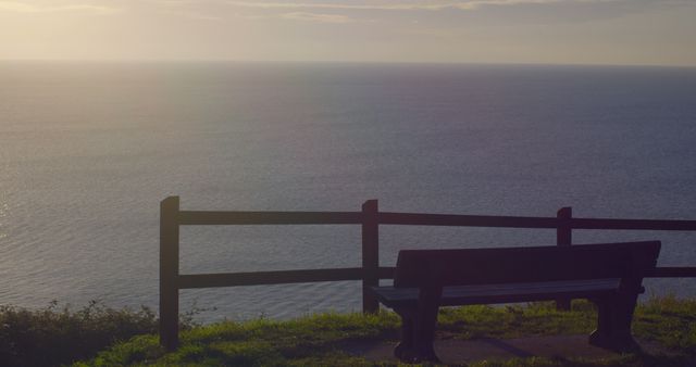 Empty bench facing vast ocean at sunset, summarizing peaceful solitude. Perfect for concepts like reflection, relaxation, and taking a break from daily life. Can be used in travel promotions, mental health blogs, or scenic backdrop designs.
