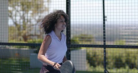 Woman playing padel on sunny outdoor fenced court holding paddle in light purple polo