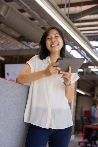 Smiling asian businesswoman using tablet in open-plan office