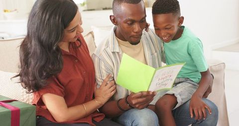 Father reading handmade father's day card with smiling son and partner on couch