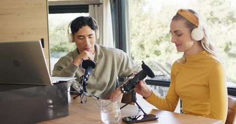 Young duo recording podcast at home studio with laptop, condenser microphones and headphones