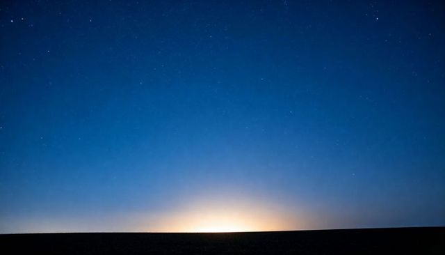 Night desert horizon with starry sky and soft luminous glow above flat silhouette