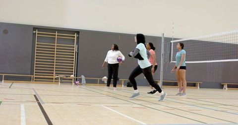 Diverse women's volleyball team practicing indoors, indian woman lunging in mint headscarf