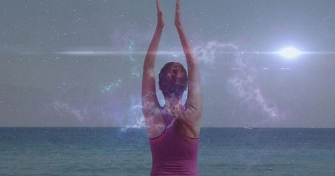 Practicing beach yoga at horizon: woman stretching overhead against cosmic seascape