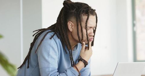 Focused professional with dreadlocks working on laptop in bright minimalist workspace