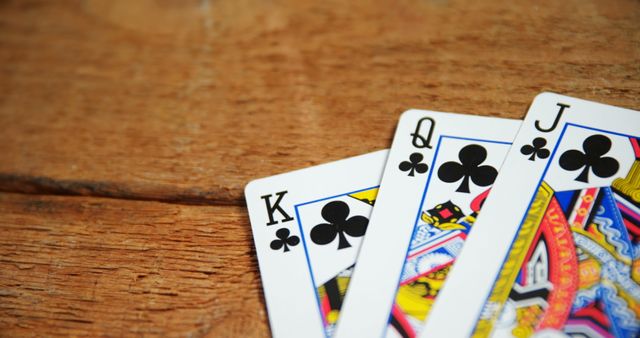 Close-up view of a set of three playing cards, including the King, Queen, and Jack of Clubs, laid out on a wooden table. This image can be used for illustrating themes related to card games, gambling, poker, and leisure activities. It is suitable for use in blogs, articles, and marketing materials for casinos, card game strategies, and entertainment.