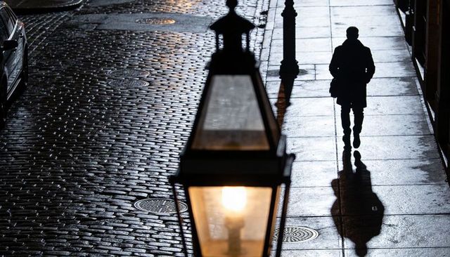 Solitary silhouette walking on wet cobblestone sidewalk under warm lantern light at night
