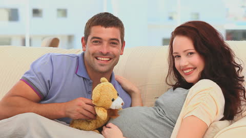 Happy Couple Expecting Child At Home With Teddy Bear