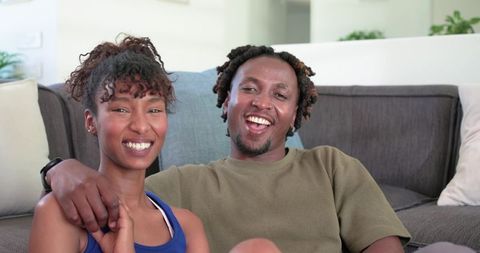 African american couple relaxing on sofa smiling together showing fitness band