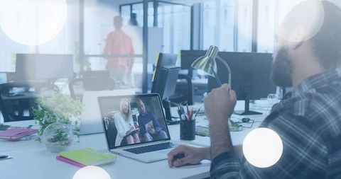 Bearded worker joining remote video meeting at modern open-plan office desk with laptop