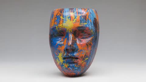 Rotating painted ceramic mask revealing glossy blue, orange and yellow splatter loop video