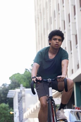 African american cyclist riding road bike through urban street gripping drop handlebars
