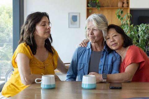 Comforting senior woman with adult companions at table, caregiving and emotional support