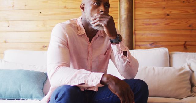 Senior african american man spending time in log cabin touching his mouth and thinking. Log cabin and lifestyle concept.