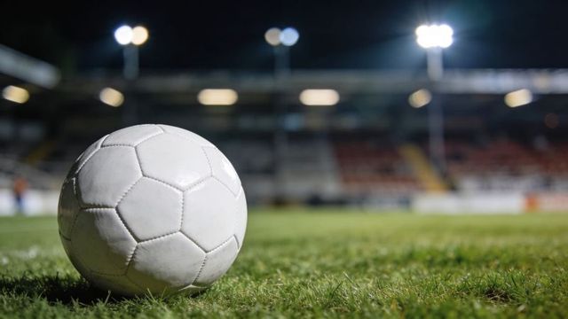 White soccer ball resting on grass pitch under stadium floodlights at night, closeup