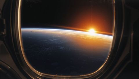Sunrise over earth from capsule window with thin blue limb curved horizon golden glow