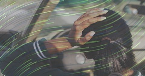 Indian woman touching hair while sitting in car with green streaked glass reflections
